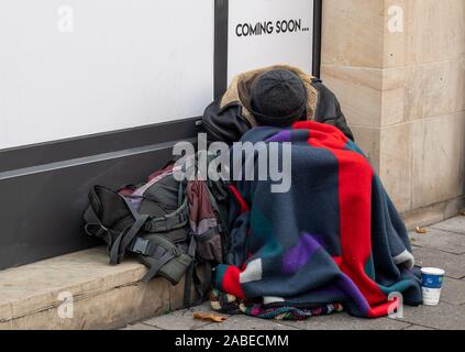 Munich, Allemagne. 26 Nov, 2019. Une personne sans-abri est assis au bord de la route en face d'une boutique dans le centre-ville et dort. Crédit : Peter Kneffel/dpa/Alamy Live News Banque D'Images