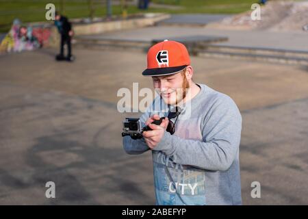 Un jeune teenage lad la capture des images de ses amis, à Stoke skate Plaza skatepark à l'aide d'une caméra GoPro et d'action de l'extension Banque D'Images