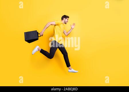 Full Size photo de beau mec haute vitesse saut garder les paquets rushing vente shopping porter des t-shirt pantalon jaune isolé fond couleur Banque D'Images