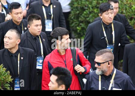 Joueur de tennis Serbe Novak Djokovic, l'une en rouge, est entouré par la sécurité et les fans sur sa façon de se préparer à double masculin Banque D'Images