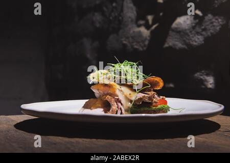 Beau plat appétissant avec de la viande de boeuf rôti et jetons sur la plaque blanche dans le restaurant de style loft. La cuisine fusion. Banque D'Images