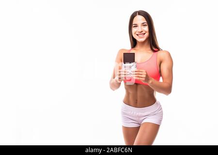 Faim et gourmand femme fitness interrompu son alimentation. Portrait of young girl eating chocolate bar tout en isolé sur fond blanc. Mauvaise Banque D'Images