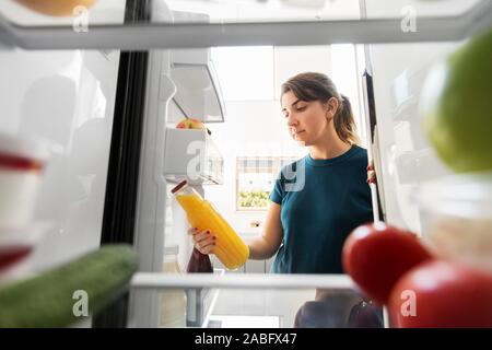 Femme tenant une bouteille de jus à partir d'un réfrigérateur à la maison Banque D'Images