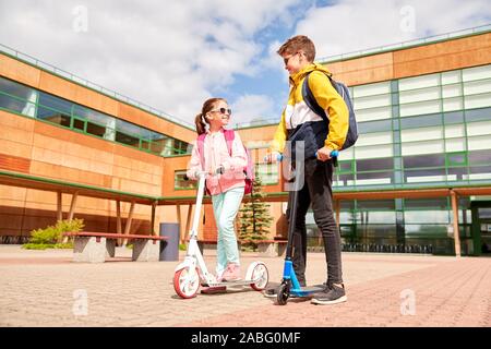 Heureux les enfants de l'école avec des sacs et des scooters Banque D'Images