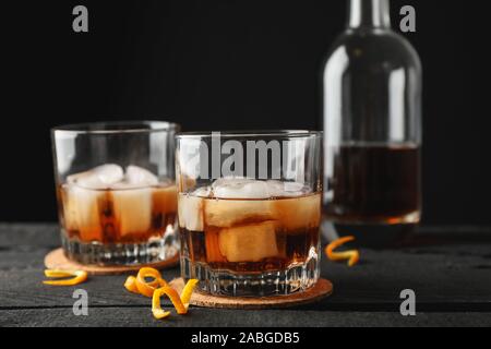 Verres de whisky avec les pelures d'orange et de la glace sur fond de bois avec une bouteille, de l'espace pour le texte Banque D'Images