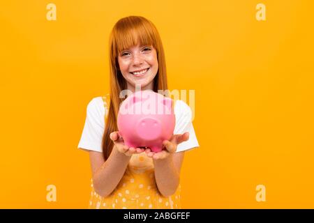 Red-haired girl holding a Piggy Bank dans les mains sur l'arrière-plan Banque D'Images