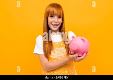 Red-haired girl holding a Piggy Bank dans les mains sur un fond jaune Banque D'Images