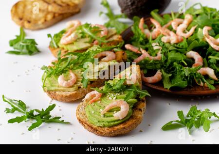 Remise en forme en bonne santé l'alimentation. Toasts à l'avocat, crevettes et salade de roquette sur fond blanc. Une bonne nutrition Banque D'Images