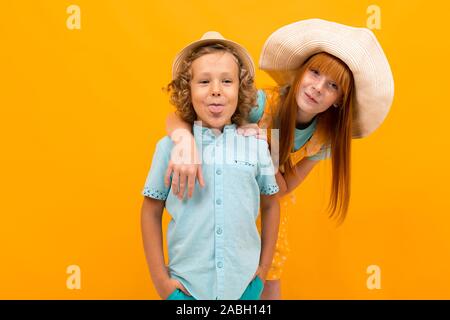 Jeune fille rousse dans un chapeau d'été se profile derrière un garçon sur un fond jaune Banque D'Images