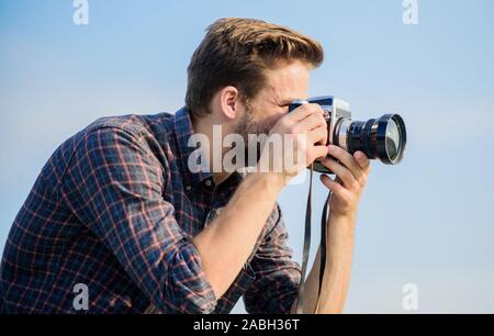 Reporter la prise de photo. Hipster photographe. Tir Blogger vlog. Guy extérieur fond de ciel bleu. Beau blogger guy meilleur appareil photo rétro. Des réglages manuels. Billet d'un blogueur. L'équipement vintage. Banque D'Images