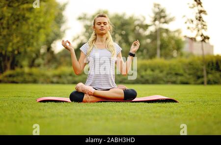 Young woman practicing yoga pose au parc sur un beau terrain vert Banque D'Images