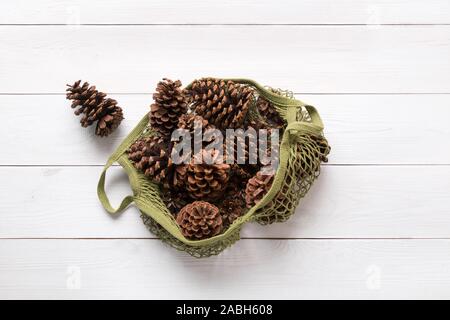 Zéro déchets maison de vacances de Noël. Matériau naturel pour le bricolage, des pommes de pin en vert eco coton blanc sac sur planche de bois. Eco friendly Noël. Vue de dessus, Banque D'Images