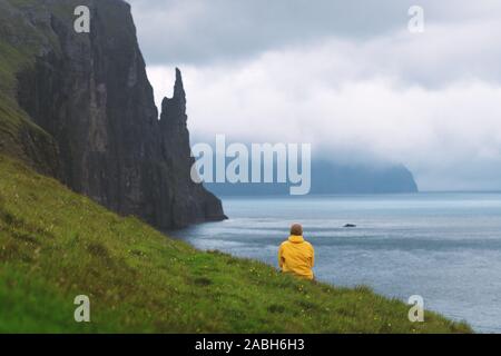 Touriste à yellow jacket porte sur les falaises d'Trollkonufingur Fabricants sorcières de vue. Vagar et l'Île, Îles Féroé, Danemark. Banque D'Images