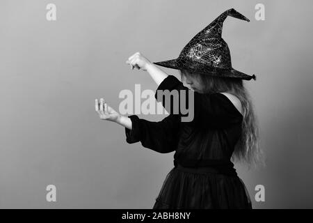 Kid en noir chapeau de sorcière, robe et visage sérieux. Magicien en costume. Fille essaie de mettre quelque chose sur l'orthographe, isolé sur fond vert, l'espace de copie. Maison de vacances d'automne et d'Halloween concept Banque D'Images