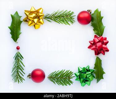 Cadre de Noël. Rouge, jaune, vert s'incline sur un fond blanc. Feuilles de houx et de branches de sapin. Des boules de Noël. Banque D'Images