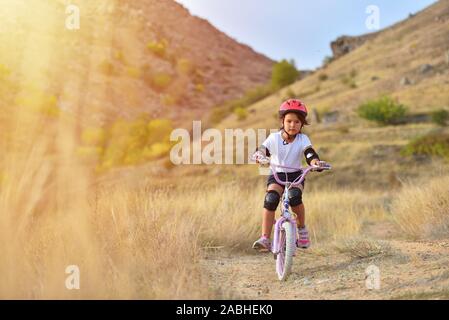 Happy kid girl de 7 ans s'amuser dans le parc de l'automne avec un vélo sur belle journée d'automne. Casque de vélo enfant portant Active Banque D'Images