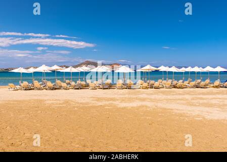Chaises longues avec des parasols sur la plage d'Agios Georgios, station balnéaire très prisée sur l'île de Naxos, Grèce. Banque D'Images