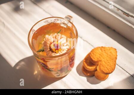 Thé aux herbes. Une tasse en verre avec plateau se tient sur le rebord. Des biscuits en forme de coeur Banque D'Images