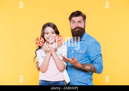 Petite fille et papa tenir sucette colorés. été vibes. famille heureuse. cheerful sur dessert. candy shop. enfance heureuse. Fille et père de manger des bonbons. hipster barbu homme est bon père. le bonheur. Banque D'Images