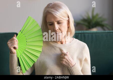 Personnes âgées surchauffé woman sitting on couch forme green fan Banque D'Images