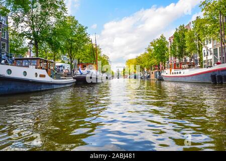 Au niveau de l'eau vue depuis un bateau d'excursion à l'automne d'un immeuble rempli de canal bateaux et péniches à Amsterdam, Pays-Bas. Banque D'Images