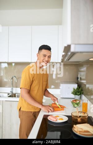 Happy young man cutting vegetables in kitchen Banque D'Images