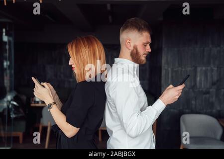 Les jeunes se tenir avec le dos à l'autre avec un smartphones dans les mains. Banque D'Images