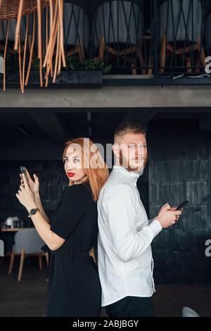 Les jeunes se tenir avec le dos à l'autre avec un smartphones dans les mains. Banque D'Images