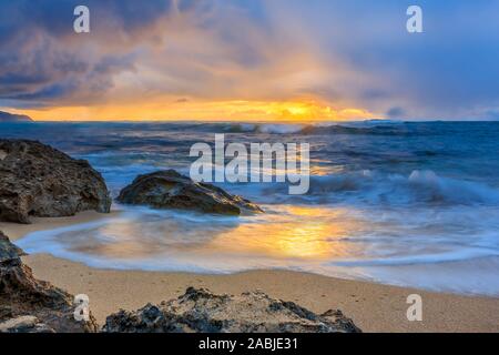 Vagues roulant sur une plage de rochers avec un magnifique coucher de soleil et la pluie à l'arrière-plan à North Shore, Oahu, Hawaii, long exposure Banque D'Images