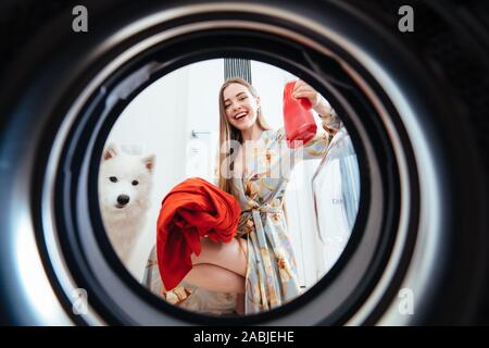 Jeune femme à la maison met la robe dans le sèche linge. Banque D'Images