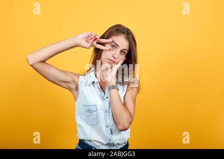 Plate jeune femme faisant le geste de la victoire, en gardant la main sur la joue, le sommeil Banque D'Images