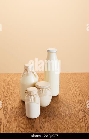 De savoureux produits laitiers biologiques dans des bouteilles sur la table rustique en bois isolé sur beige Banque D'Images