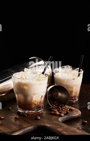 Cocktail russe blanc dans les verres avec paille sur planche de bois avec des grains de café et shaker isolated on black Banque D'Images