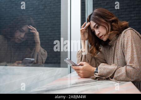 Appuyée à la jeune femme à son smartphone et avoir des maux de tête, se sentir triste, d'une inquiétude à propos de problème Banque D'Images