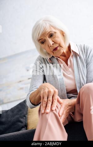 Low angle view of senior woman having douleur au genou et assis sur un canapé dans l'appartement Banque D'Images