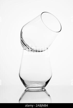 Deux verres à whisky debout comme une pyramide sur une surface miroir sombre et un fond blanc Banque D'Images