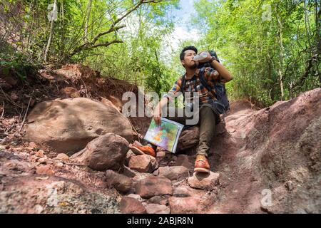 Sac à dos homme fatigué traveler avec le repos et le dirking dans la forêt naturelle de l'eau Banque D'Images