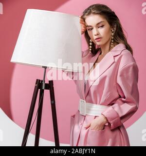 Jolie jeune fille debout avec la main dans la poche près de marbre blanc et rose sur la lampe Banque D'Images