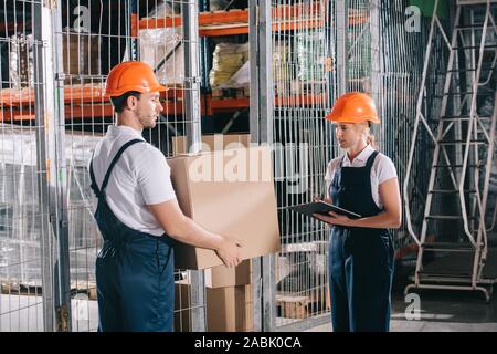 Loader holding cardboard box près de workwoman writing on clipboard Banque D'Images