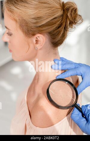 Portrait de dermatologist examining patient de la peau avec une loupe en clinique Banque D'Images