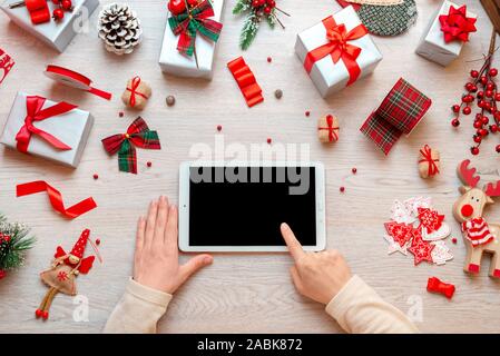 Utilisation de fille tablette avec écran vide pour immersive, app ou web site promotion, entouré de décorations de Noël cadeaux nad. Mise à plat, vue supérieure de la composition Banque D'Images