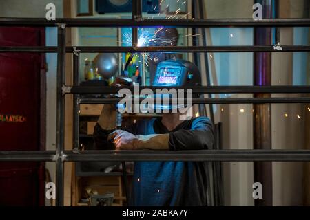 Vue de face d'un concepteur soudeur portant un casque et wokring sur un projet en soudant une construction métallique tout en rendant les étincelles de soudage dans son w Banque D'Images