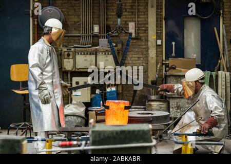 Deux artisans dans des vêtements d'argent au sable faire technique de coulage de l'aluminium en fusion liquide de couleur argent dans un moule dans un industri Banque D'Images