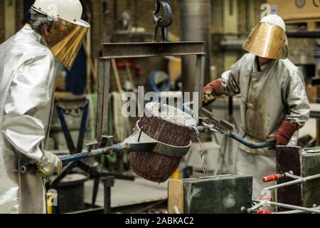 Deux artisans dans des vêtements d'argent au sable faire technique de coulage de l'aluminium en fusion liquide de couleur argent dans un moule dans un induastr Banque D'Images