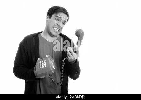 Studio shot of young man holding persan en colère et à à l'ancien téléphone contre isolé sur fond blanc Banque D'Images