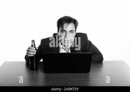 Studio shot of Persian woman drunk tout en tenant une bouteille de bière et à la recherche à l'appareil photo avec un ordinateur portable sur une table en bois Banque D'Images