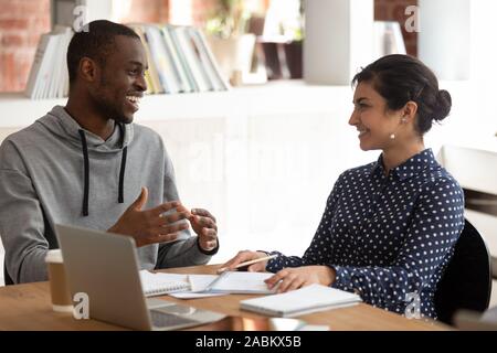 Cheerful black guy discuter des idées de projet avec smiling indian girl. Banque D'Images