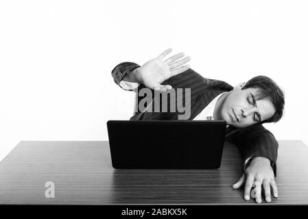 Studio shot of young businessman sleeping Persan tout en montrant la main stop sign avec ordinateur portable sur une table en bois Banque D'Images