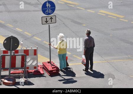 Deux personnes âgées sont debout au bord de la grand site en construction pour le tunnel à Luise- Kiesselbach-Platz à un franchissement routier, en attendant le feu vert des feux de circulation. [Traduction automatique] Banque D'Images