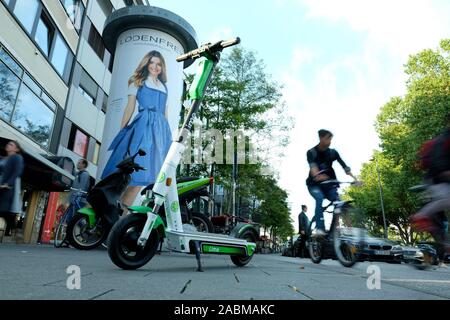 Garé sur un trottoir de scooter électrique le fournisseur la chaux dans Munich. Un cycliste est à cheval sur la piste cyclable qui le longe. [Traduction automatique] Banque D'Images